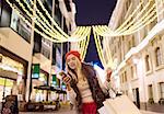 Young female shopper reading smartphone texts on street at xmas, London, UK