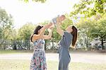 Young woman and mother holding up baby girl in park