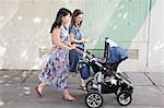 Young woman and mother and pushing baby carriage along street