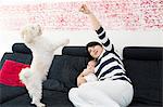 Mature woman and baby granddaughter playing with dog on sofa