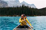 Front view of mid adult man paddling canoe, looking away, Moraine lake, Banff National Park, Alberta Canada