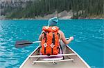 Rear view of mid adult woman with orange colour backpack paddling canoe, Moraine lake, Banff National Park, Alberta Canada