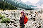 Side view of mid adult woman on rocky landscape carrying backpack looking at camera smiling, Moraine Lake, Banff National Park, Alberta Canada