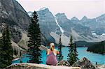 Rear view of mid adult woman on cliff edge looking at alevated view of Moraine lake, Banff National Park, Alberta Canada