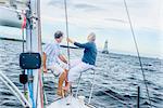 Mature couple on bow of sailboat looking away towards lighthouse