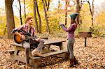 Young woman photographing guitar playing boyfriend in autumn forest