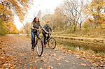 Happy young couple cycling along riverside in autumn