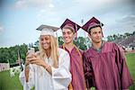 Young female and male graduates taking smartphone selfie at graduation ceremony