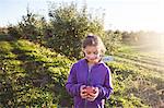 Girl in orchard holding apple looking down smiling
