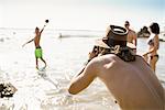 Young man photographing friends playing  American football  in sea at Newport Beach, California, USA