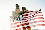 Rear view of young couple wrapped in American flag on Newport Beach, California, USA