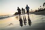 Rear view of adult friends running on beach at sunset, Newport Beach, California, USA