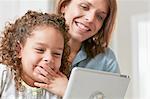 Low angle view of mother and daughter using digital tablet, hand over mouth smiling