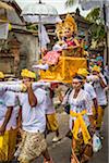 Woman being carried in a raised chair by people in a parade at a cremation ceremony for a high priest in Ubud, Bali, Indonesia