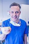 Dentist in blue scrubs holding mouth model