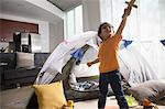 Young boy in living room using tent as den, arm raised, looking up, holding sword