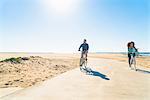 Couple cycling along pathway at beach