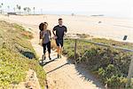 Couple running along pathway by beach