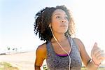 Mid adult woman running by beach, wearing earphones