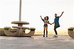 Couple using rollerskates and skateboard, holding hands, smiling