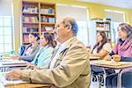 Male and female mature students listening from class desks