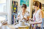 Female potter explaining to mature student making pot on potters wheel