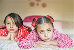 Portrait of two sisters lying on bed gazing