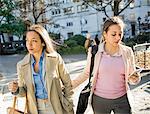 Young adult female twins walking arm in arm through city park