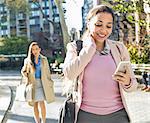 Young woman reading smartphone texts whilst walking through city park