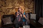 Male couple sitting on sofa, taking self portrait using smartphone