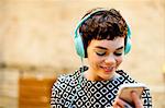 Mid adult woman, wearing headphones, looking at smartphone, smiling