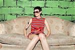 Portrait of mid adult woman, wearing sunglasses, sitting on worn sofa