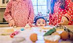 Boy in kitchen making cookies with sisters peeking over kitchen counter looking at camera