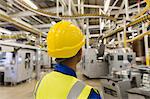 Worker in hard-hat watching printing press conveyor belts and machinery in printing plant