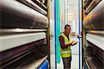 Engineer with clipboard examining printing press machinery