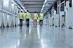 Workers in reflective clothing walking past large paper spools in printing plant