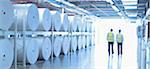 Workers in reflective clothing walking along large paper spools in printing plant