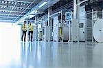 Workers walking along machinery in factory