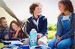 Smiling brother and sister with insulated drink container at campsite