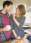 Girlfriend feeding boyfriend croissant in kitchen