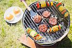 Overhead view of hamburgers and vegetable skewers on barbecue grill