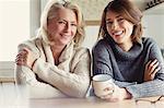 Portrait smiling mother and daughter in sweaters drinking coffee in kitchen