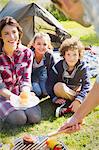 Family watching father barbecuing at campsite grill