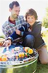 Father and son barbecuing hamburgers and vegetable skewers