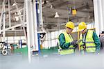 Workers in protective workwear talking with clipboard working in factory