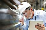 Focused engineer with digital tablet and flashlight examining part in factory