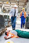 Workers running toward fallen coworker unconscious on factory floor