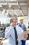 Engineer with clipboard talking on cell phone in factory