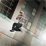 A young man breakdancing on a city sidewalk leaping in the air and striking a pose, looking at the camera.