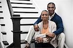 A mature couple, man and woman, sitting on the stairs together at home.